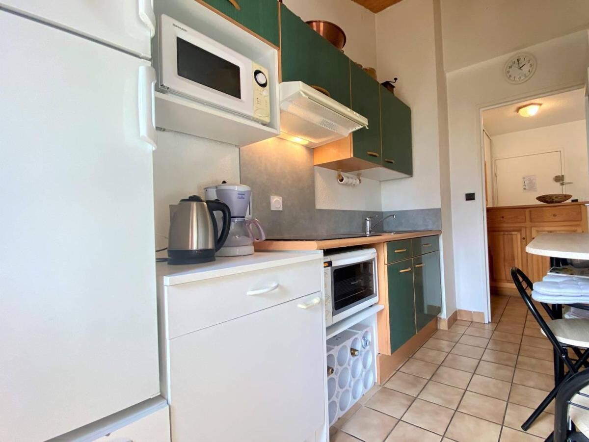 A compact kitchen with a microwave, kettle, and oven. There is a small refrigerator and a dining area with a table and chairs.