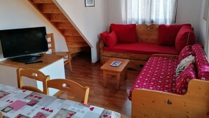Um quarto acolhedor com uma escada de madeira, um sofá vermelho, uma mesa de madeira e uma televisão.