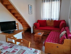 Un ambiente accogliente con una scala in legno, un divano rosso, un tavolo di legno e un televisore.