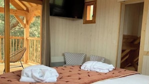 A bedroom with a large bed, a television mounted on the wall, and a balcony with a chair. - Cabane Château Luxe Jacuzzi/spa Privé - 2 à 6 Pers (Vieille-Brioude)