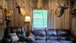 Een kamer met een houten plafond, twee leren banken, een houten salontafel en opgehangen hertenkoppen aan de muur.