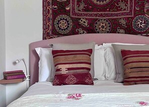 Ein Bett mit rosa Kopfteil, weißer Bettwäsche und dekorativen Kissen mit geometrischen Mustern.