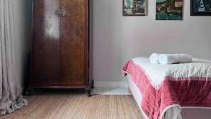 Une chambre à coucher avec une armoire en bois, un lit recouvert d’une couette rose et blanche, et trois tableaux encadrés accrochés au mur.