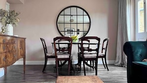 Un coin repas agrémenté d’un miroir rond, de chaises en bois, d’une table en bois et d’un fauteuil vert foncé.