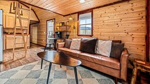Ein gemütliches Holzhaus-Interieur mit einer Couch, einem Couchtisch, einem Esstisch und einer Küchenzeile.