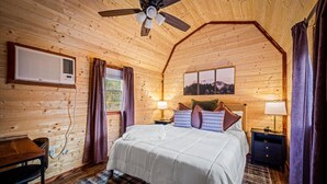 Ein gemütliches Schlafzimmer in einer Holzhütte, mit einem Bett, einem Schreibtisch und einem Deckenventilator.