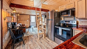 Ein Interieur einer Holzhütte mit einer Küche, die einen Kühlschrank, einen Herd, eine Mikrowelle und Holzschränke beinhaltet.
