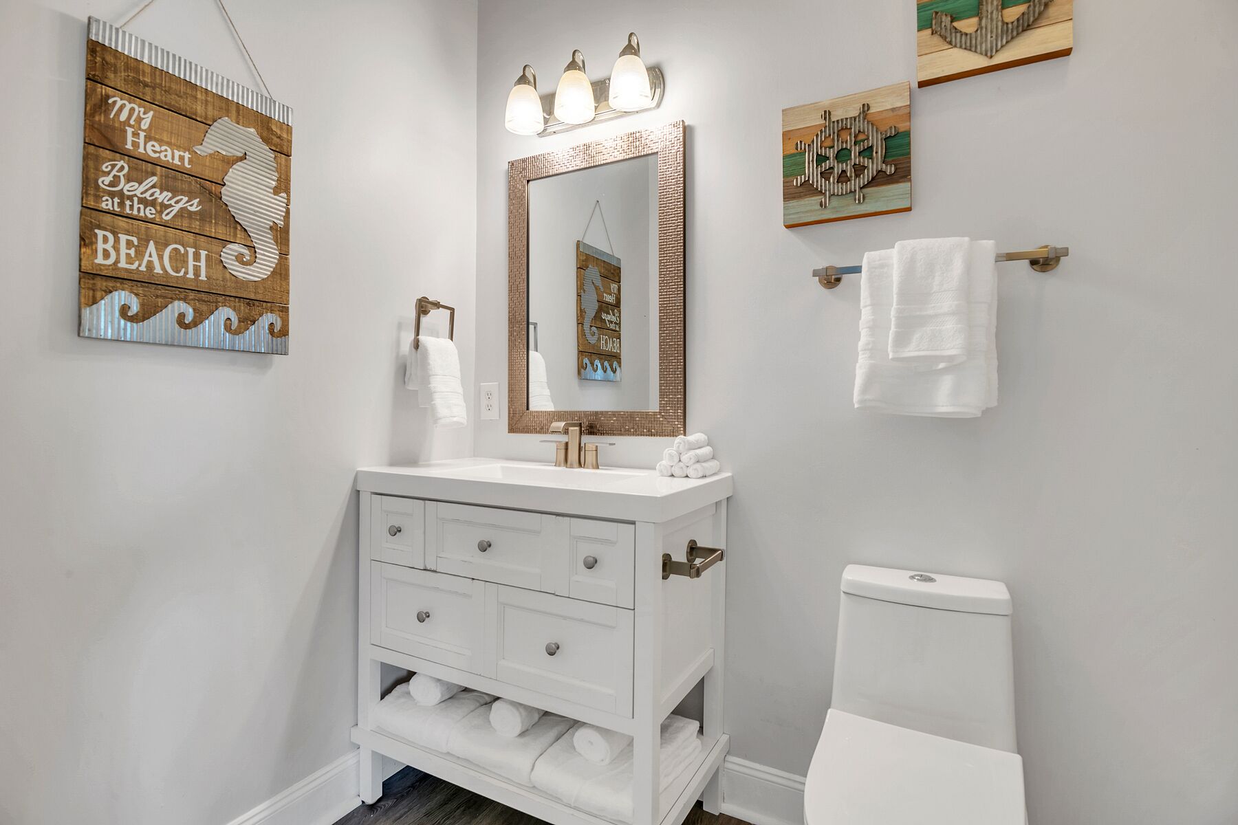 Une salle de bain avec un meuble-lavabo blanc, un miroir avec éclairage intégré, un porte-serviettes et des toilettes.
