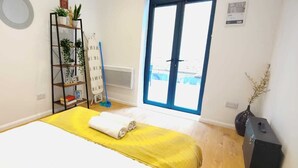 Ein Schlafzimmer mit einem Bett, einem gelben Handtuch, einem Regal mit Pflanzen, einem Mop und einem Fenster mit Blick.