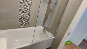 Ein Badezimmer mit einer gläsernen Duschkabine, einer weißen Badewanne und einer gefliesten Wand.