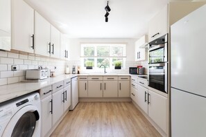 A modern kitchen with white cabinetry, a built-in washing machine, and a large window with a view of greenery.