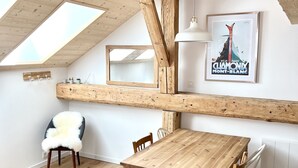 A high-ceilinged room with exposed wooden beams, a wooden dining table with chairs, a fluffy chair, and a framed picture on the wall. - Triplex In The Heart Of Chamonix (Chamonix-Mont-Blanc)