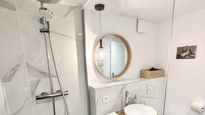 A modern bathroom with a glass shower enclosure, a round mirror, a wooden vanity, and a white sink. - Triplex In The Heart Of Chamonix (Chamonix-Mont-Blanc)