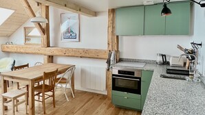 A modern kitchen with wooden beams, a dining area with a table and chairs, and green cabinets. - Triplex In The Heart Of Chamonix (Chamonix-Mont-Blanc)