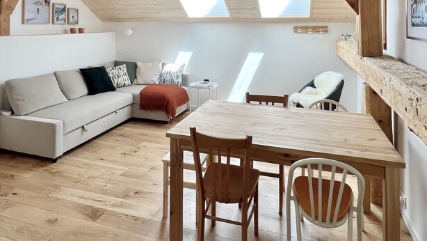 A spacious loft with a wooden floor, a dining area with a table and chairs, a sofa, and a small round table with a lamp. - Triplex In The Heart Of Chamonix (Chamonix-Mont-Blanc)