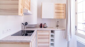 Een kleine keuken met houten kastjes, een inbouwfornuis, een spoelbak en een raam met gordijnen.