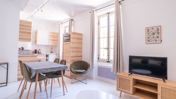 Een moderne woonkamer met een eethoek, een televisie op een houten dressoir, en een keuken op de achtergrond.