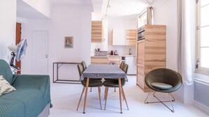 Een compacte leefruimte met een eettafel, twee stoelen, een bank en een keukenhoek.