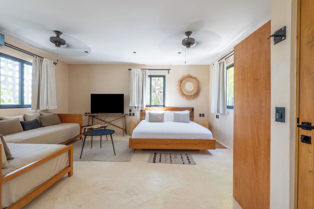A modern bedroom with a large bed, a sofa, a TV, and a ceiling fan.