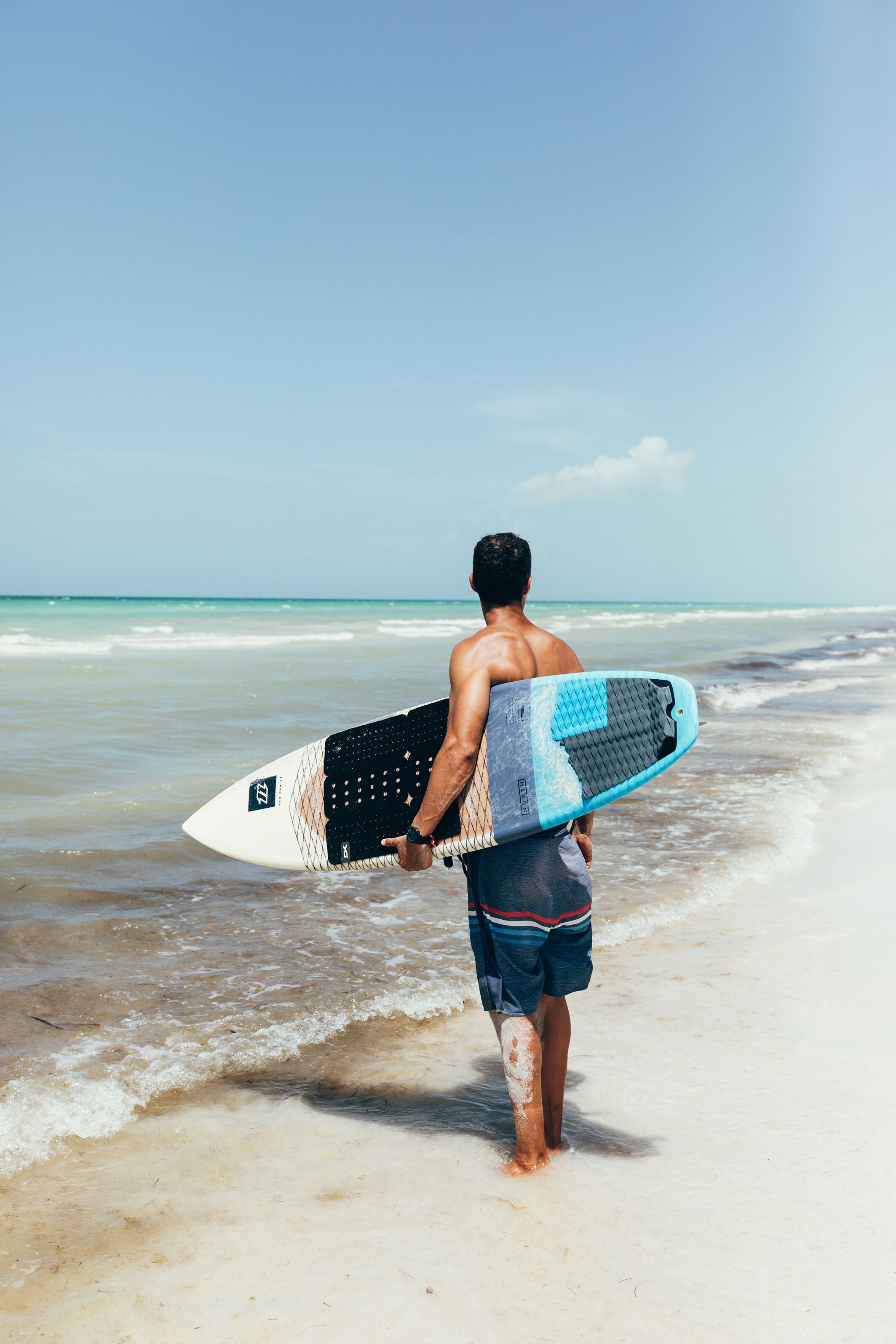 A man walking on a beach holding a surfboard.