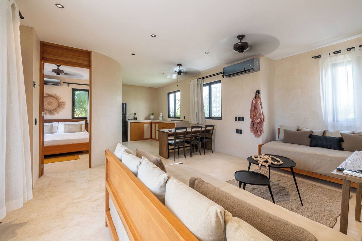 A spacious room with a bed, a sofa, a dining area, and a small kitchen.
