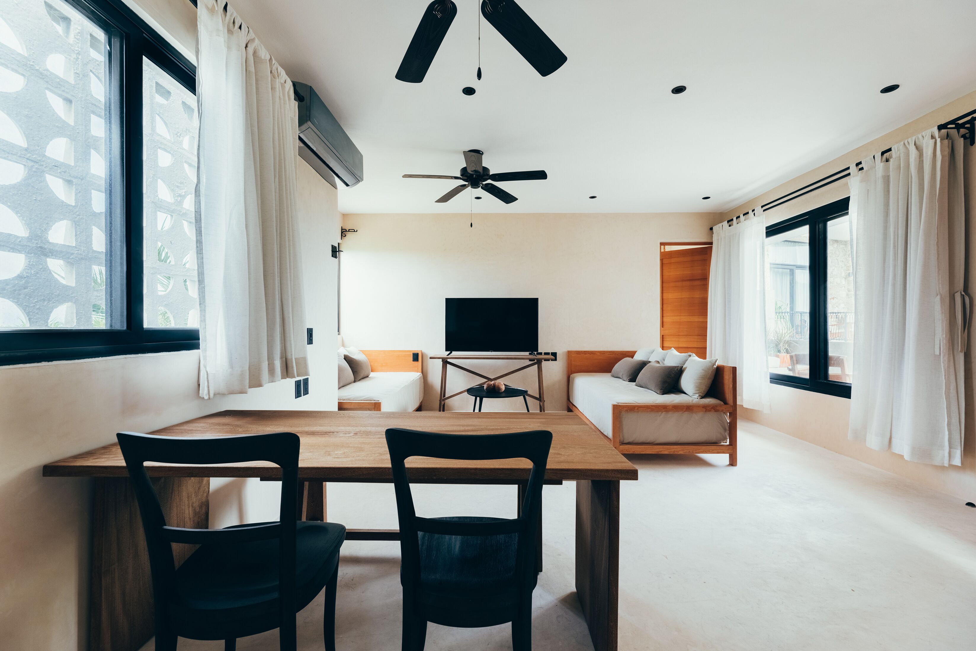 A modern living room with a wooden dining table, two chairs, a ceiling fan, and a TV on a stand.