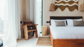 A bedroom with a wooden bed, white bedding, a woven wall hanging, and a small wooden stool.