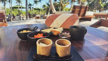 A table with a meal setup including bowls, a cup, and a spoon, set against a backdrop of a beach with palm trees and lounge chairs.