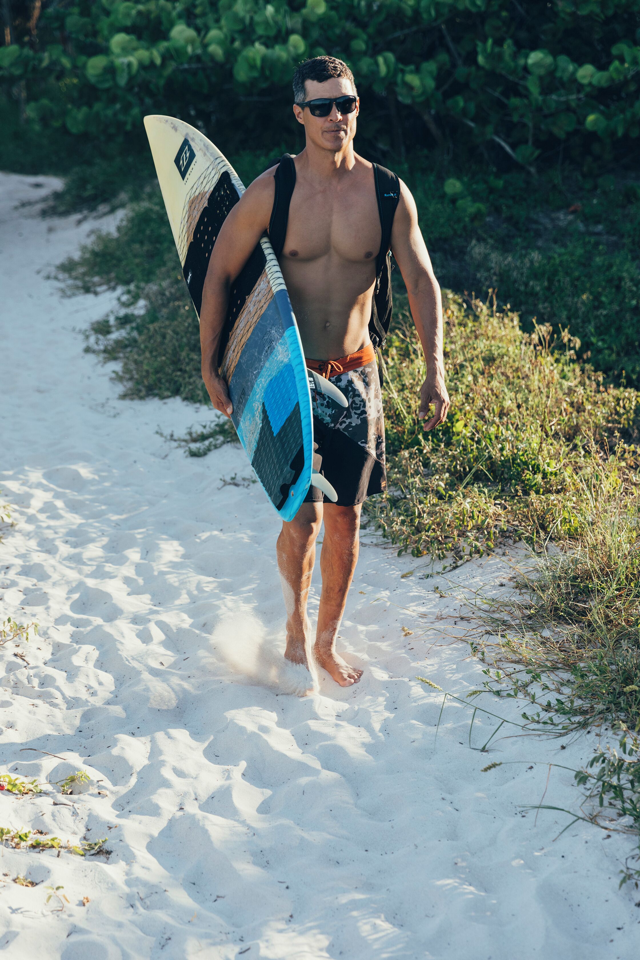 A person walking on a sandy path with a surfboard.