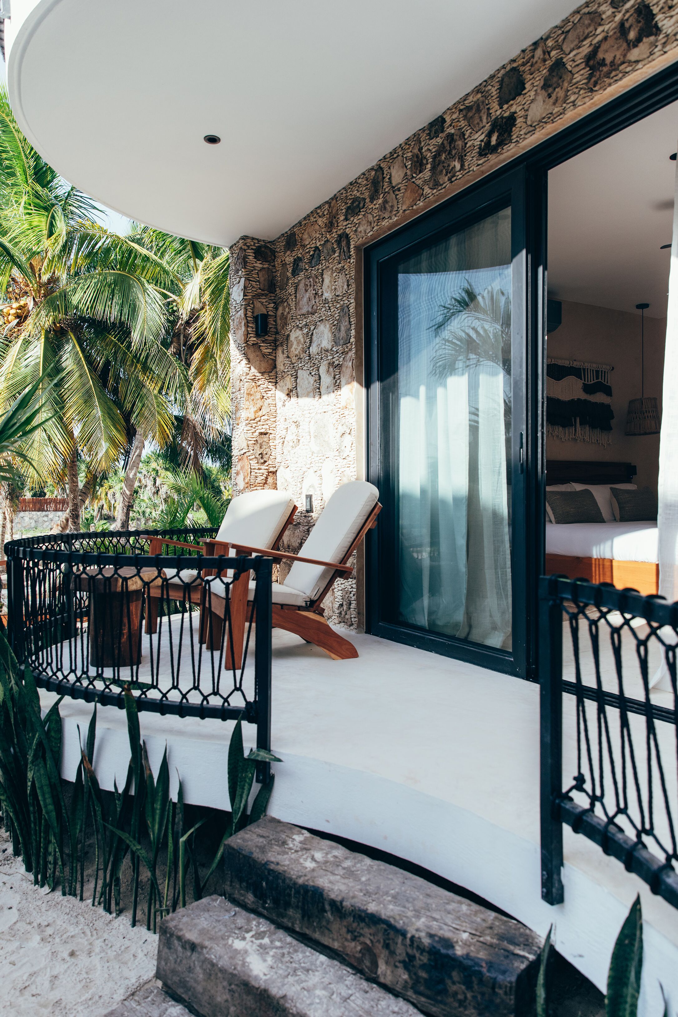 Un balcon avec un mur en pierre, un plafond blanc et une vue sur une chambre à coucher avec un lit et des rideaux.