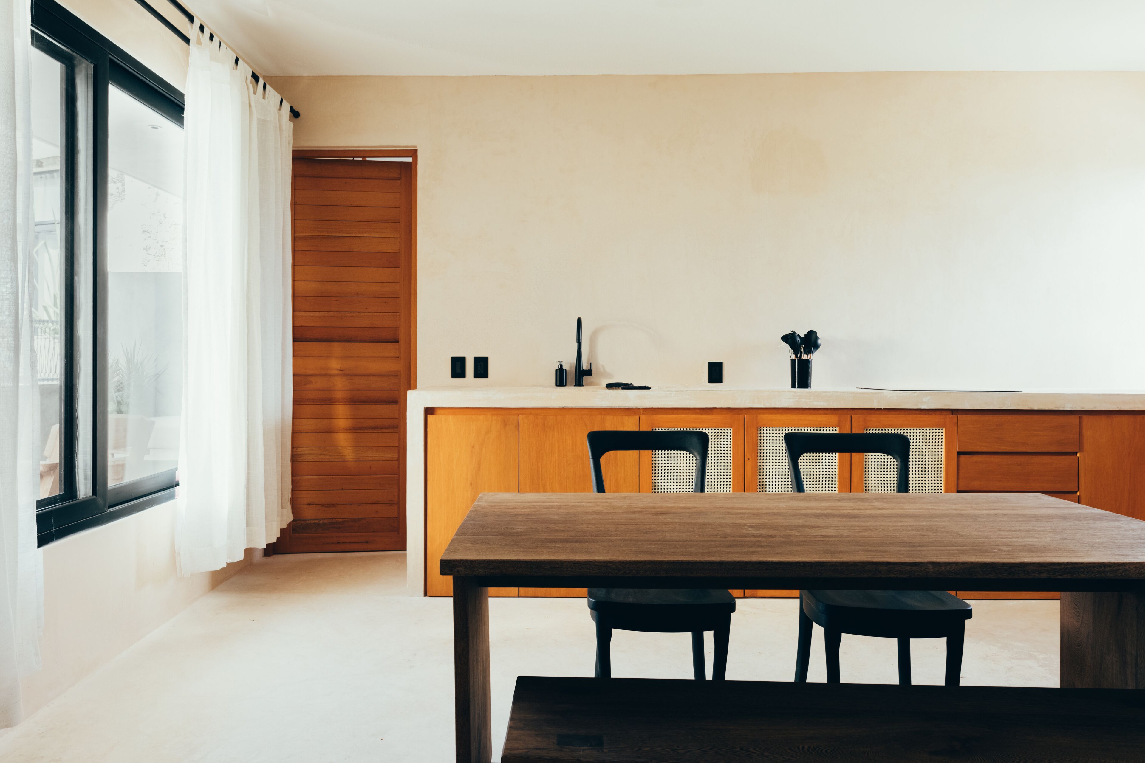 Une cuisine moderne avec des meubles en bois, un grand îlot central et deux chaises noires.