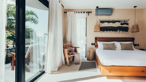 A bedroom with a large bed, a wooden headboard, a TV mounted on the wall, and a view of palm trees through the window.