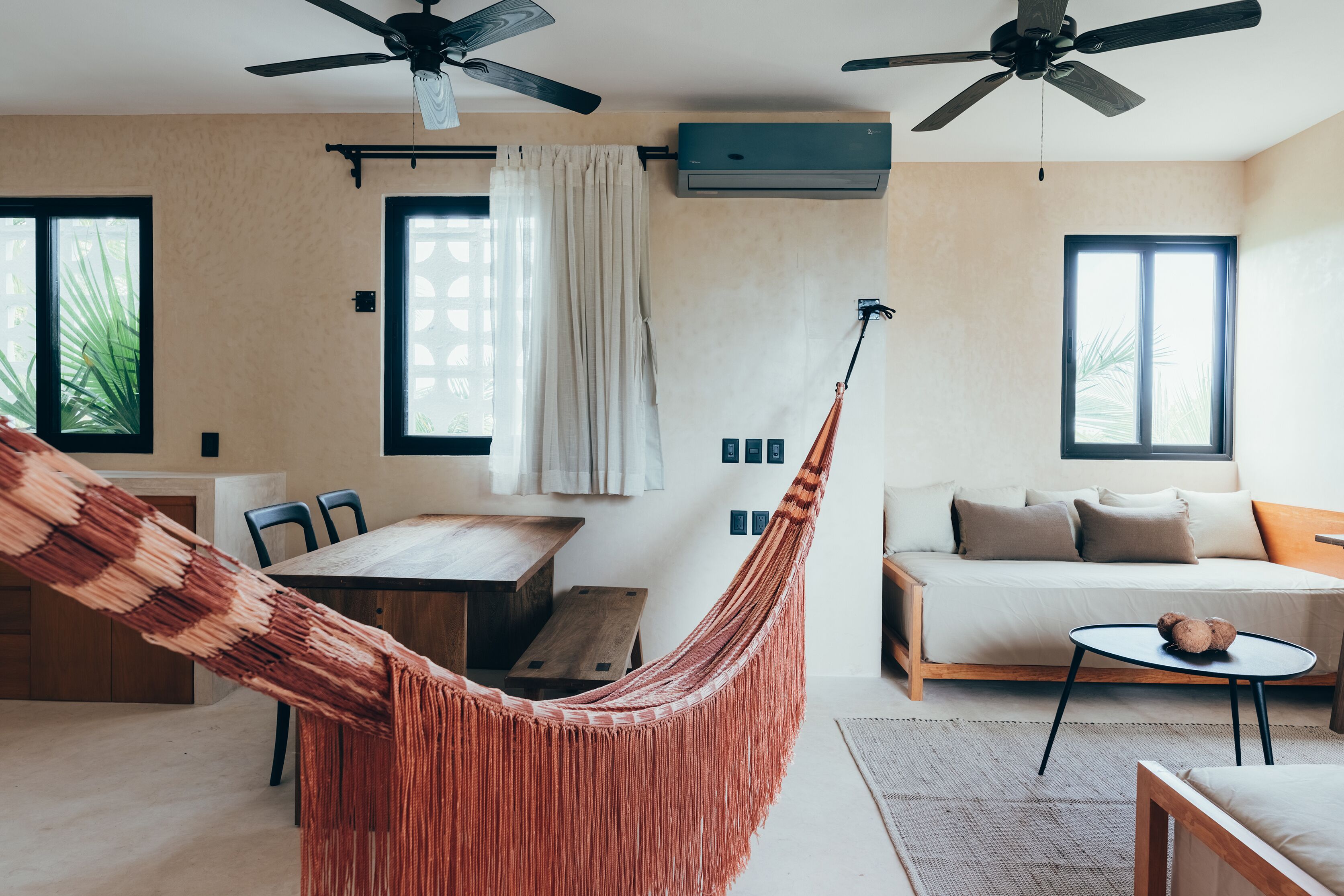 Una sala moderna con una hamaca, un sofá, una mesa de comedor y ventiladores de techo.