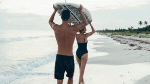 A couple walking on a beach with a surfboard.