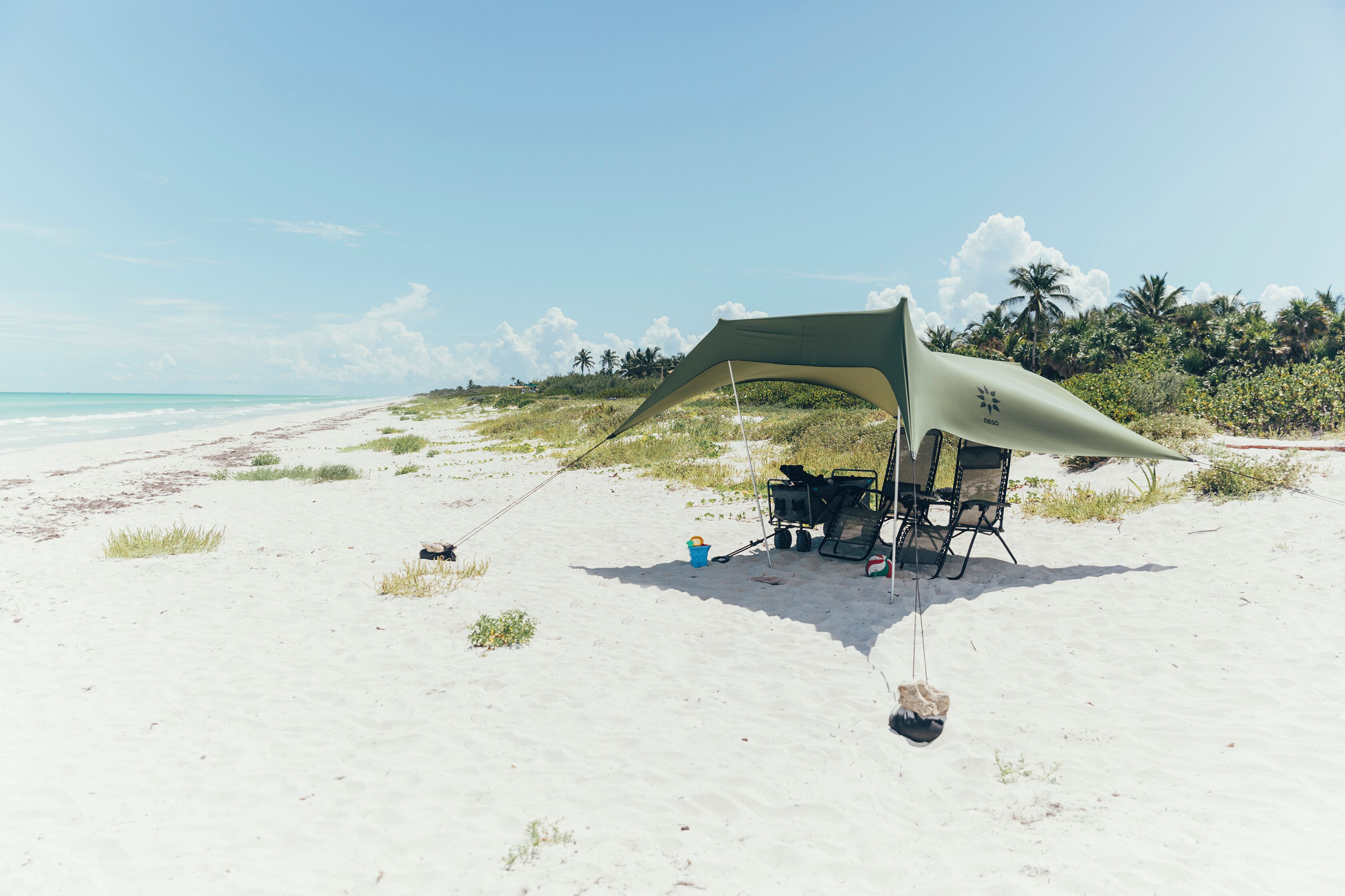 Un aménagement de camping sur la plage comprenant un auvent, des chaises de camping et une tente.