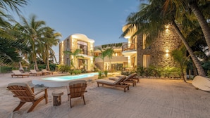 A beachfront property with a swimming pool, lounge chairs, and palm trees.