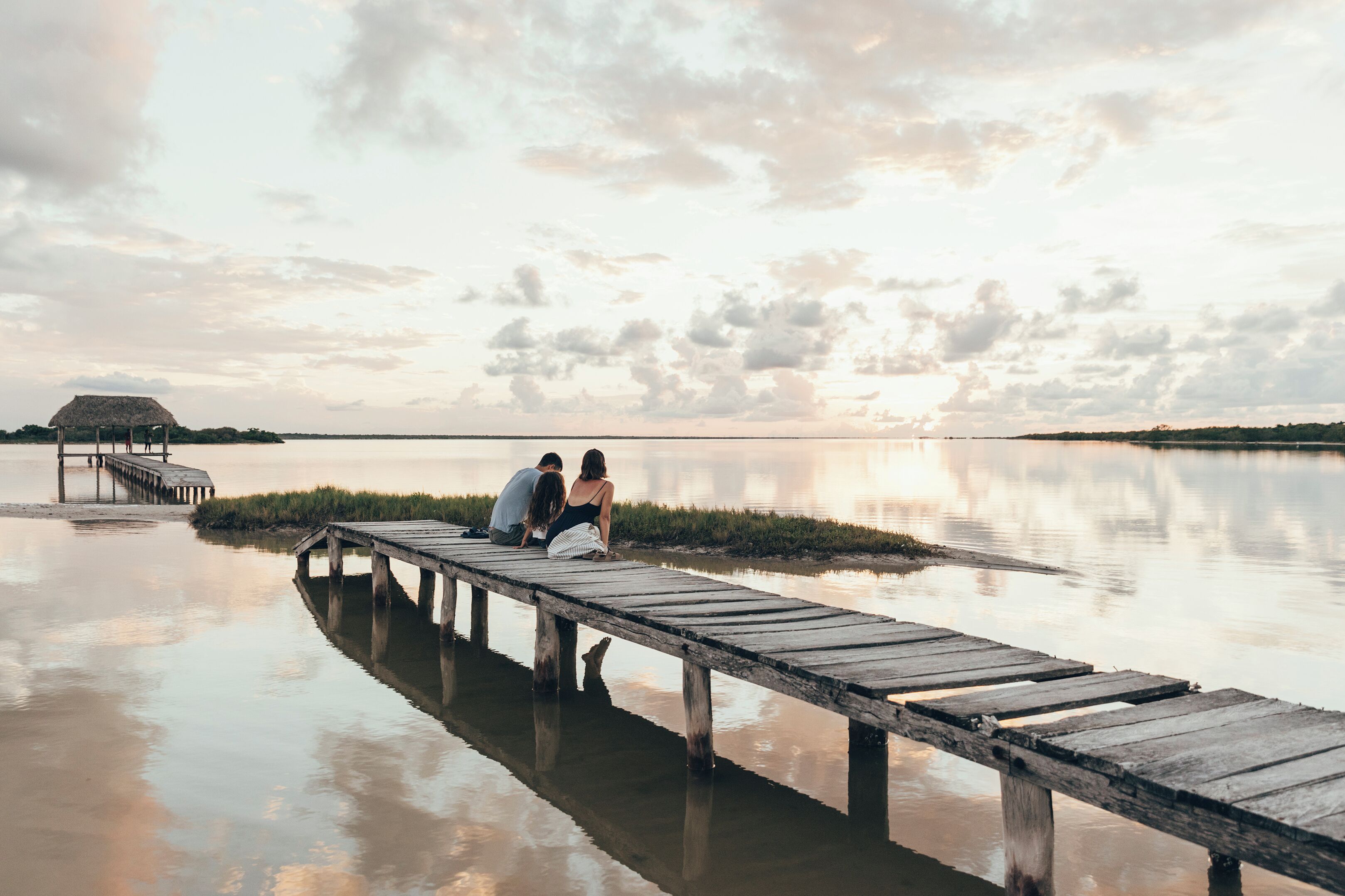 A wooden pier extending into calm water with a thatched-roof structure in the background.