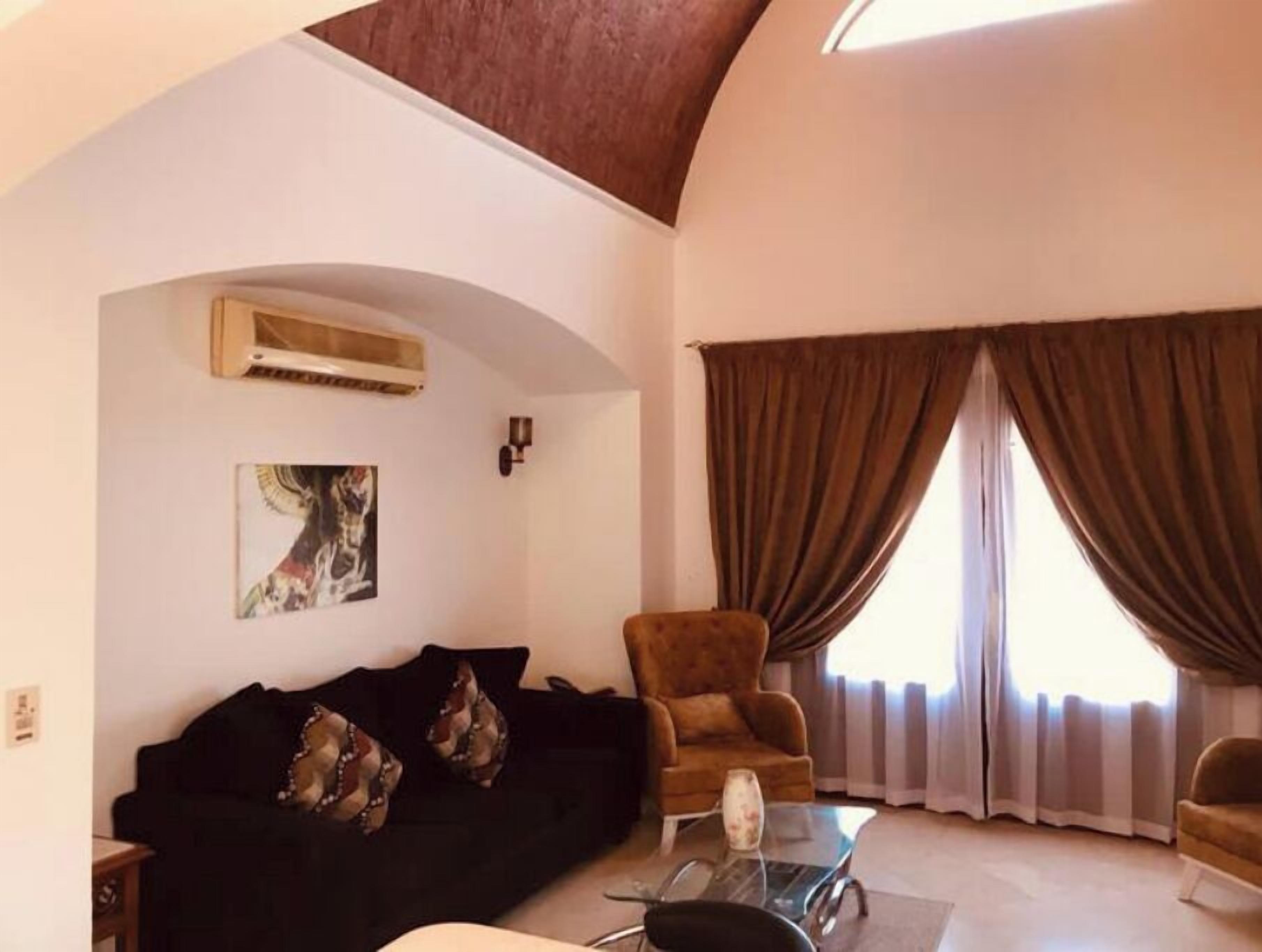 A living room with a black sofa, a brown armchair, a glass coffee table, and a painting on the wall.