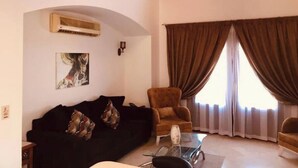 Una sala de estar con un sofá negro, un sillón marrón, una mesa de centro de vidrio y un cuadro en la pared.