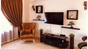 Una sala de estar con un televisor de pantalla plana grande, un sillón marrón, un mueble de entretenimiento negro y estantes decorativos con pequeñas plantas.