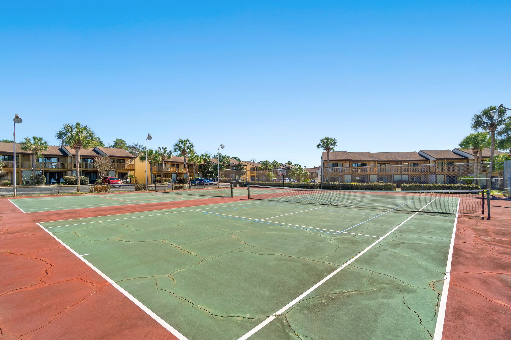 A tennis court with a net, surrounded by buildings and palm trees.