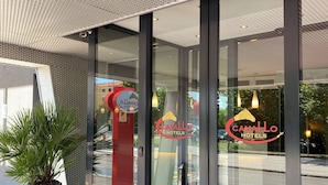 Entrada de un hotel con puertas de cristal, alfombra roja y una planta en maceta.
