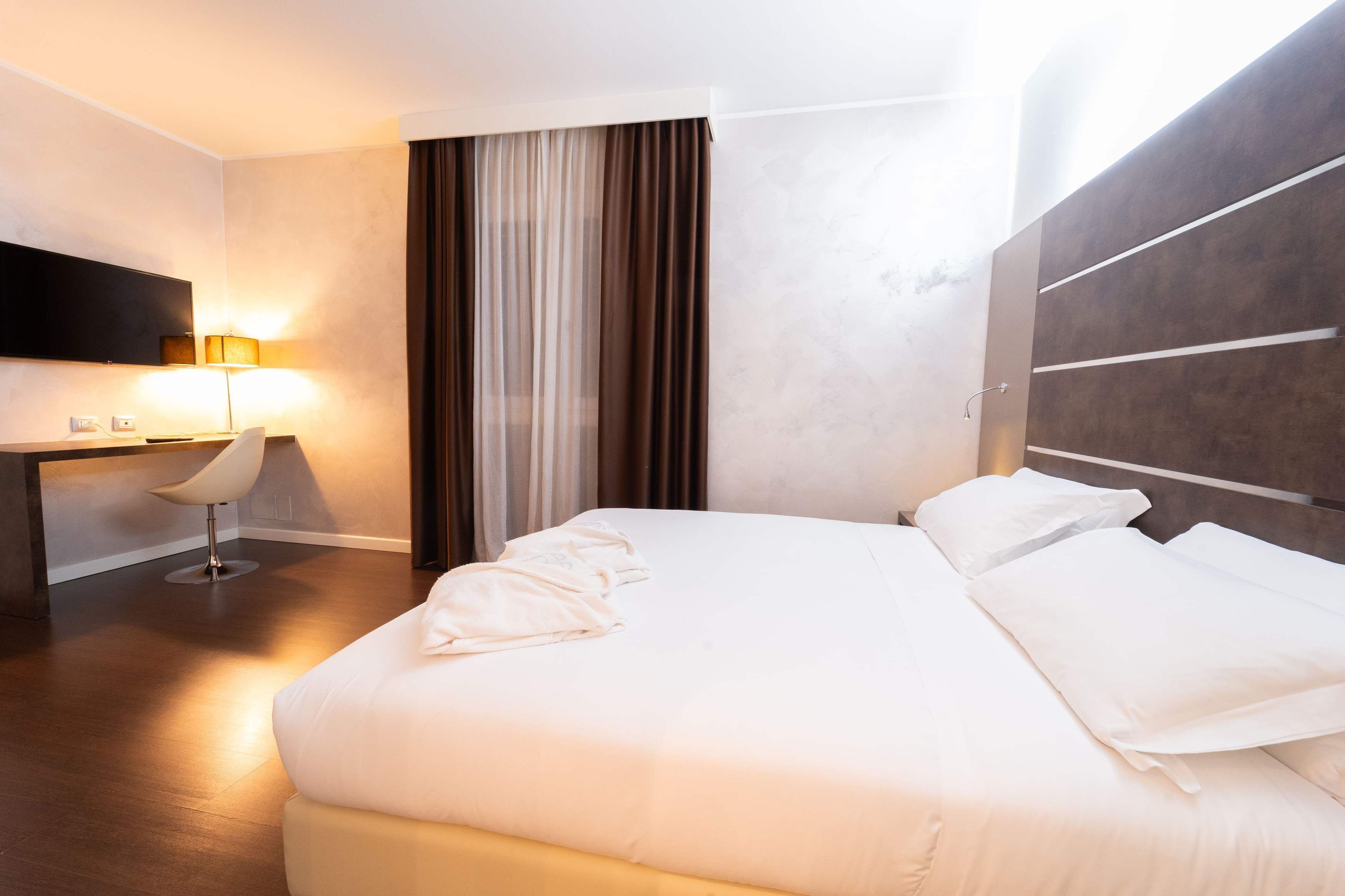 Une chambre d’hôtel avec un lit, un bureau, une chaise, une télévision et une fenêtre avec des rideaux.