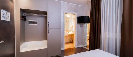 A hotel room with a bed, a wardrobe, a television, and a bathroom visible through an open door.