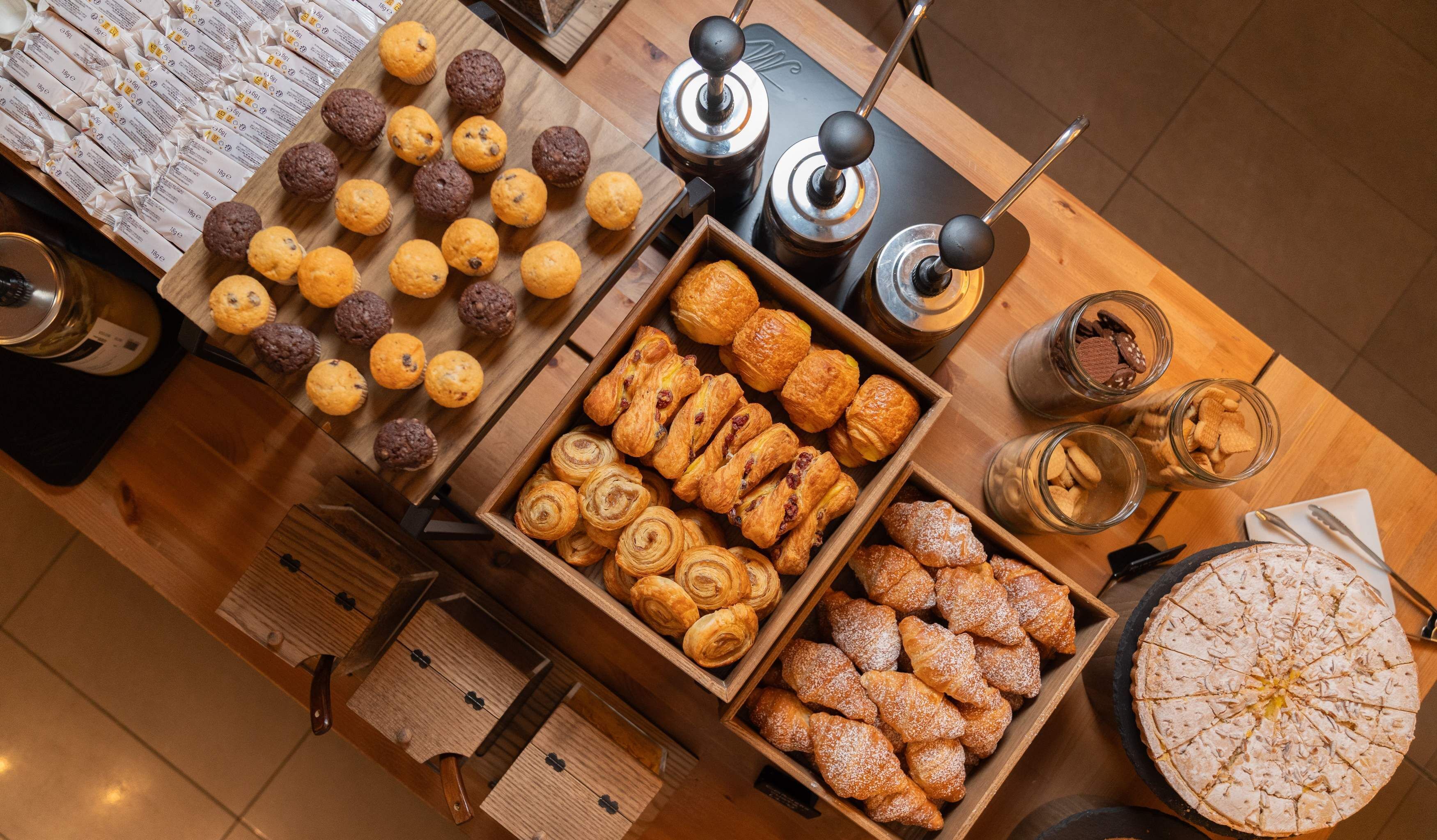 Verschiedene Backwaren, darunter Muffins, Croissants und Gebäck, stehen auf einem Holztisch.