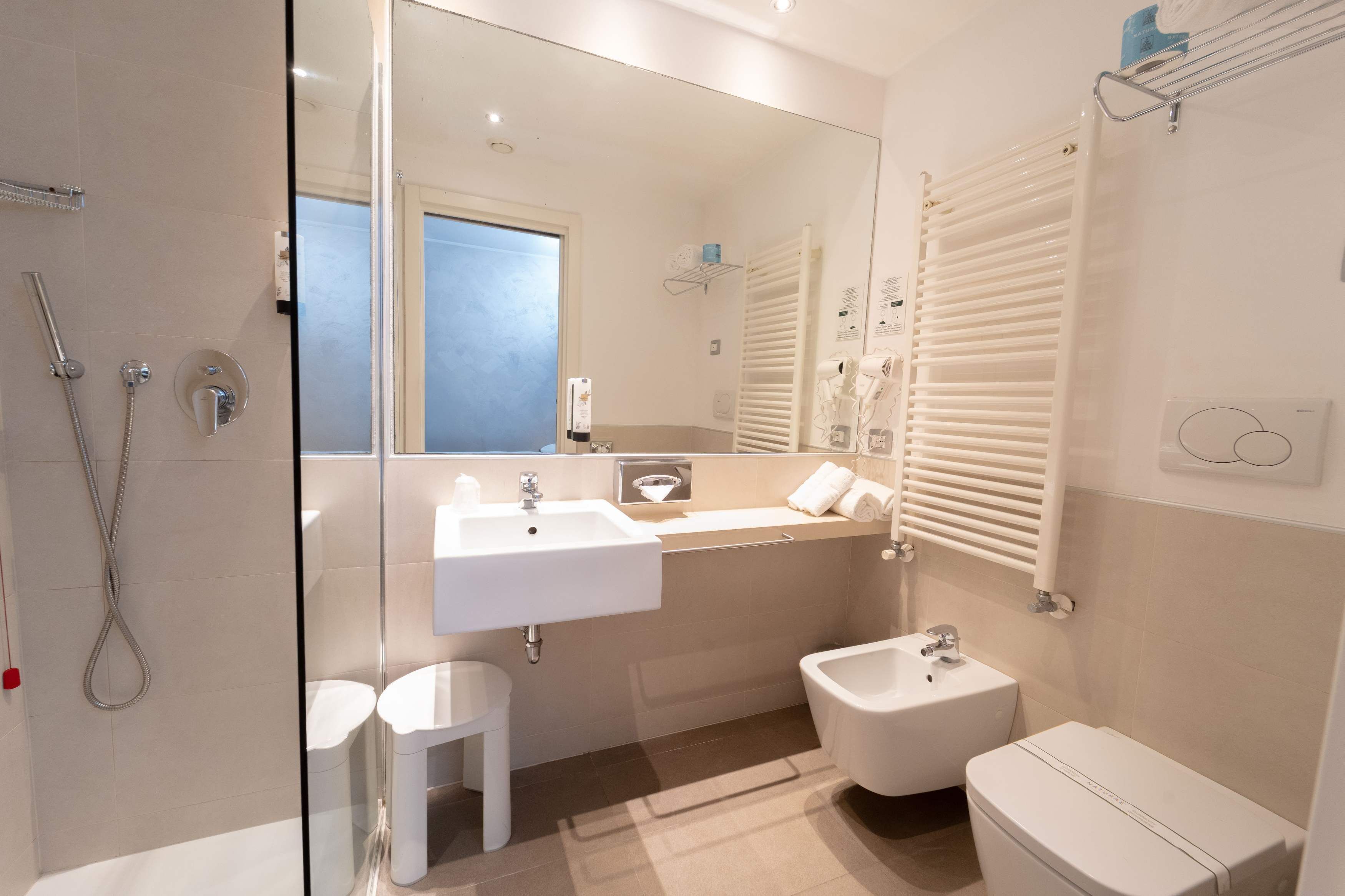 A modern bathroom with a glass shower enclosure, a double sink vanity, a bidet, and a toilet.