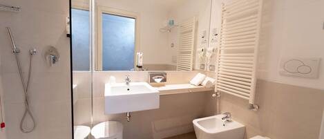 A modern bathroom with a glass shower enclosure, a double sink vanity, a bidet, and a toilet.