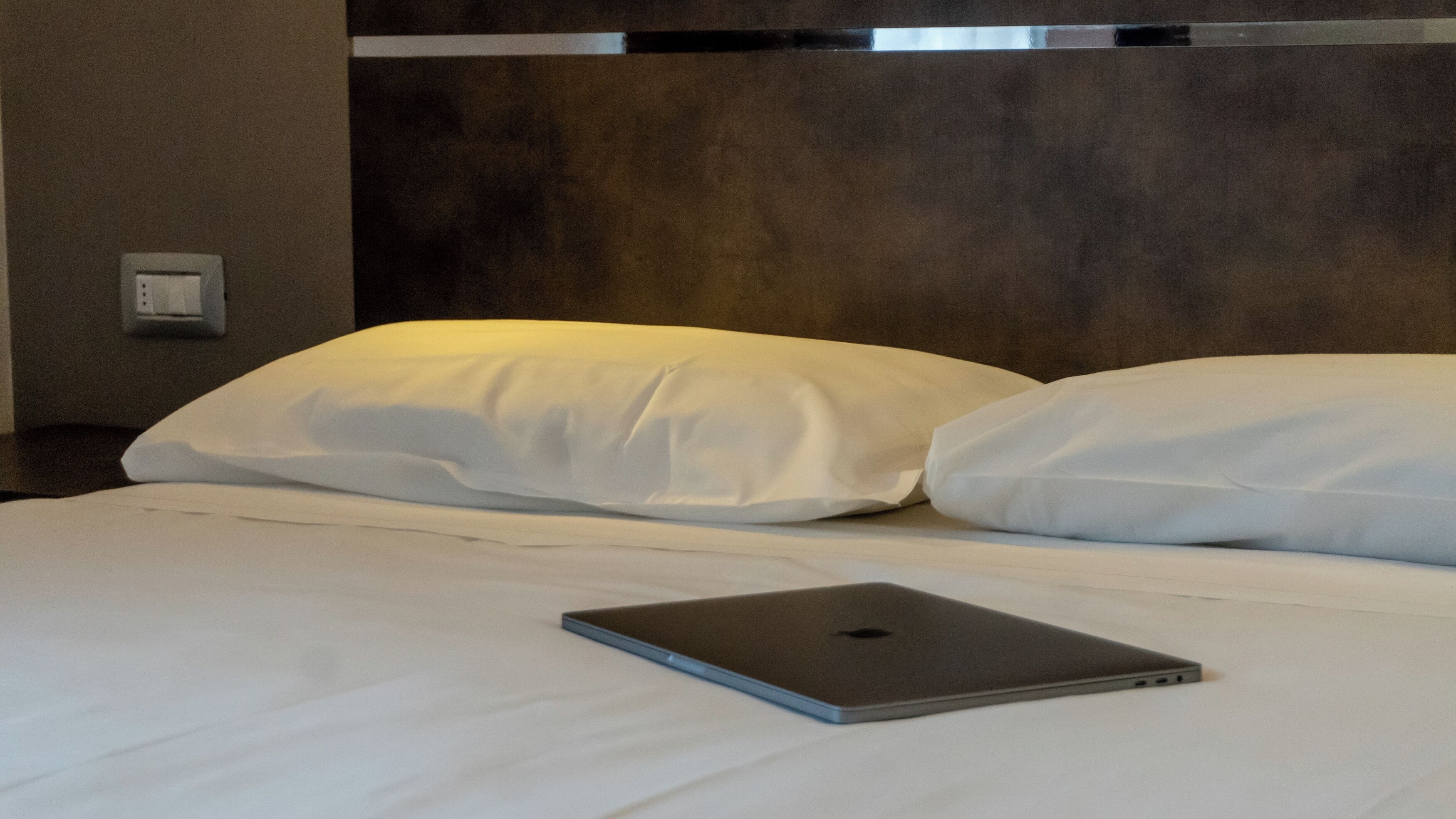 Ein ordentlich bezogenes Bett mit weißer Bettwäsche und ein Laptop darauf.
