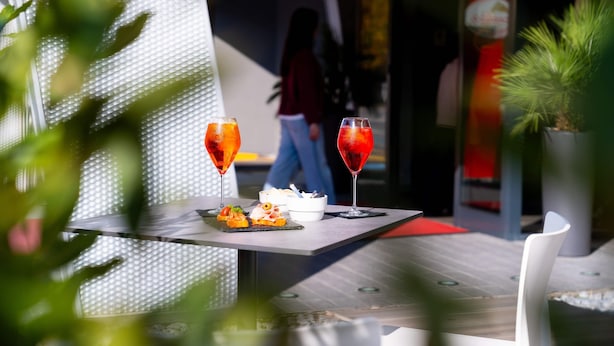 Una mesa con dos bebidas rojas y un postre, un cuenco blanco y una planta en maceta.