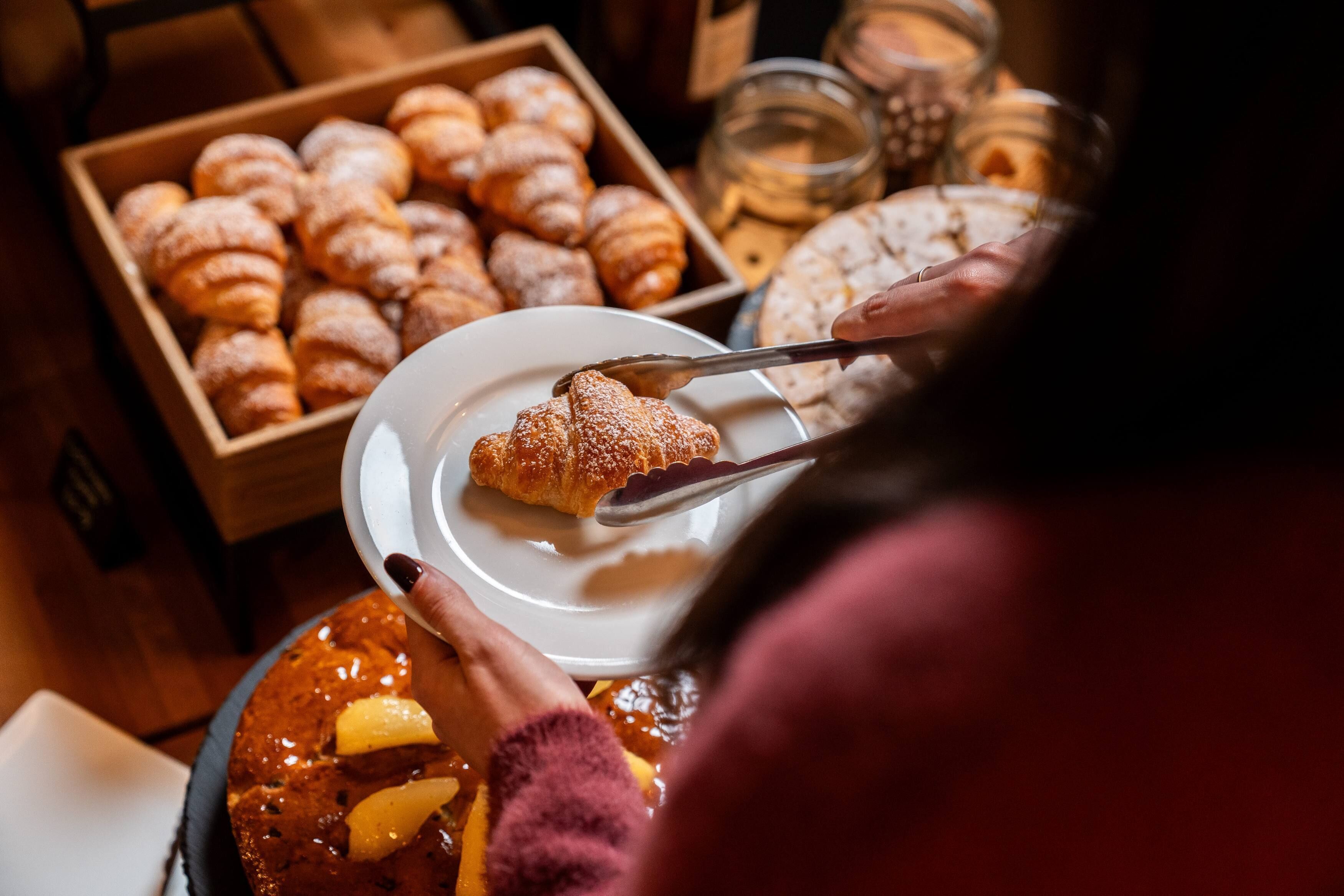 Una persona sirviendo un croissant de una caja de pasteles.